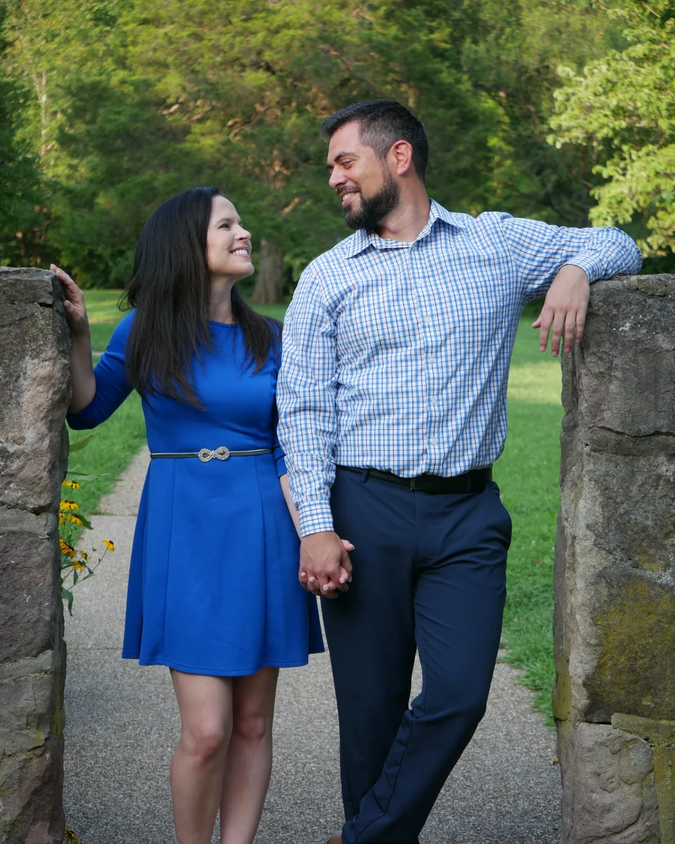 Christen and her husband smiling at each other while standing between stone pillars.